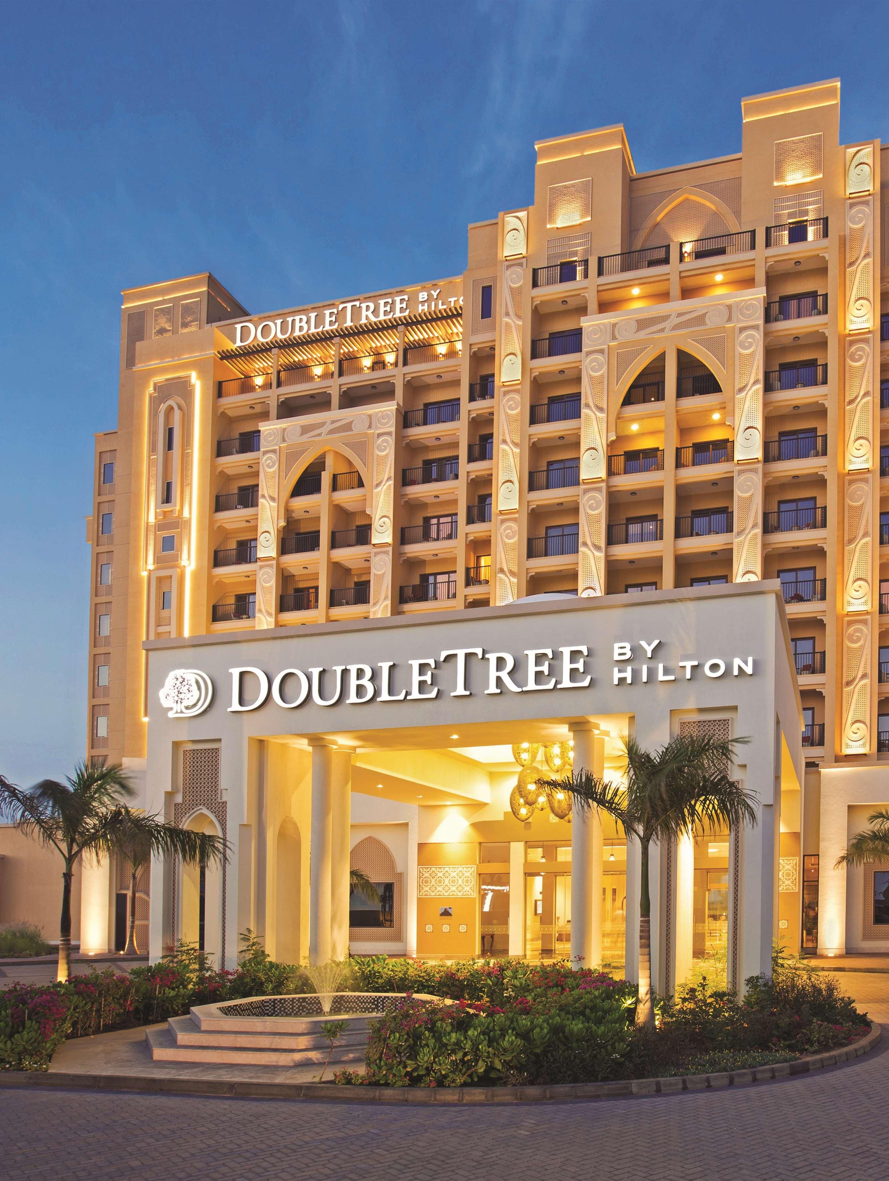 A hotel with a prominent 'DOUBLETREE BY HILTON' sign, multiple balconies, and a well-lit entrance.