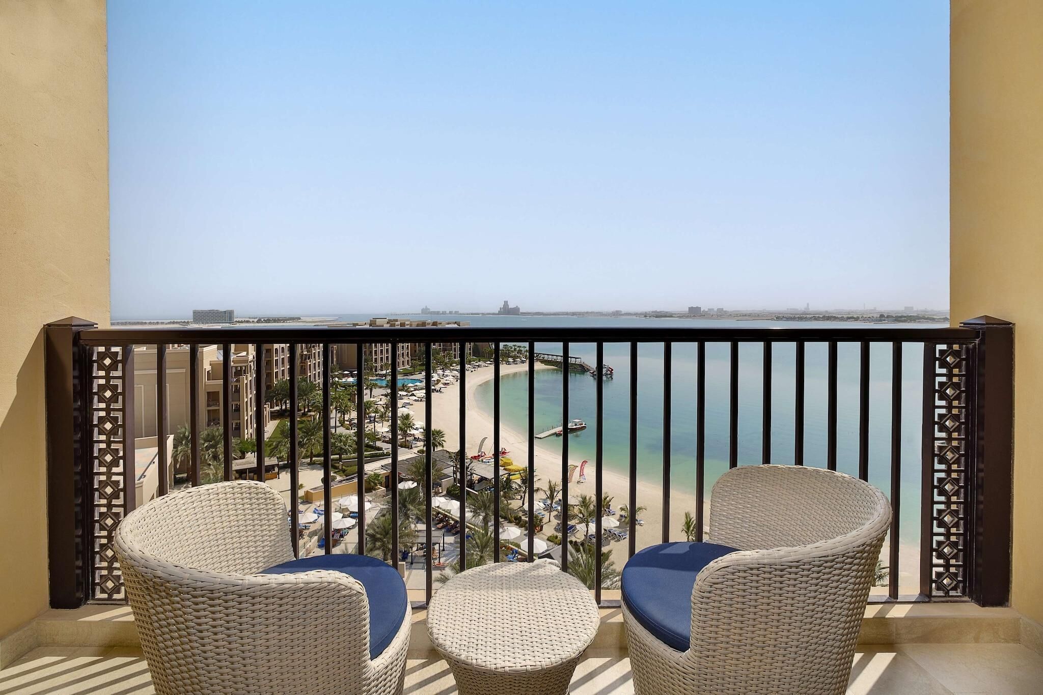 Un balcon avec des fauteuils en osier et une petite table, d’où l’on peut admirer une plage et une jetée.