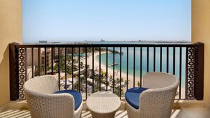 Un balcón con sillas de mimbre y una mesa, con vista a una playa y un muelle.