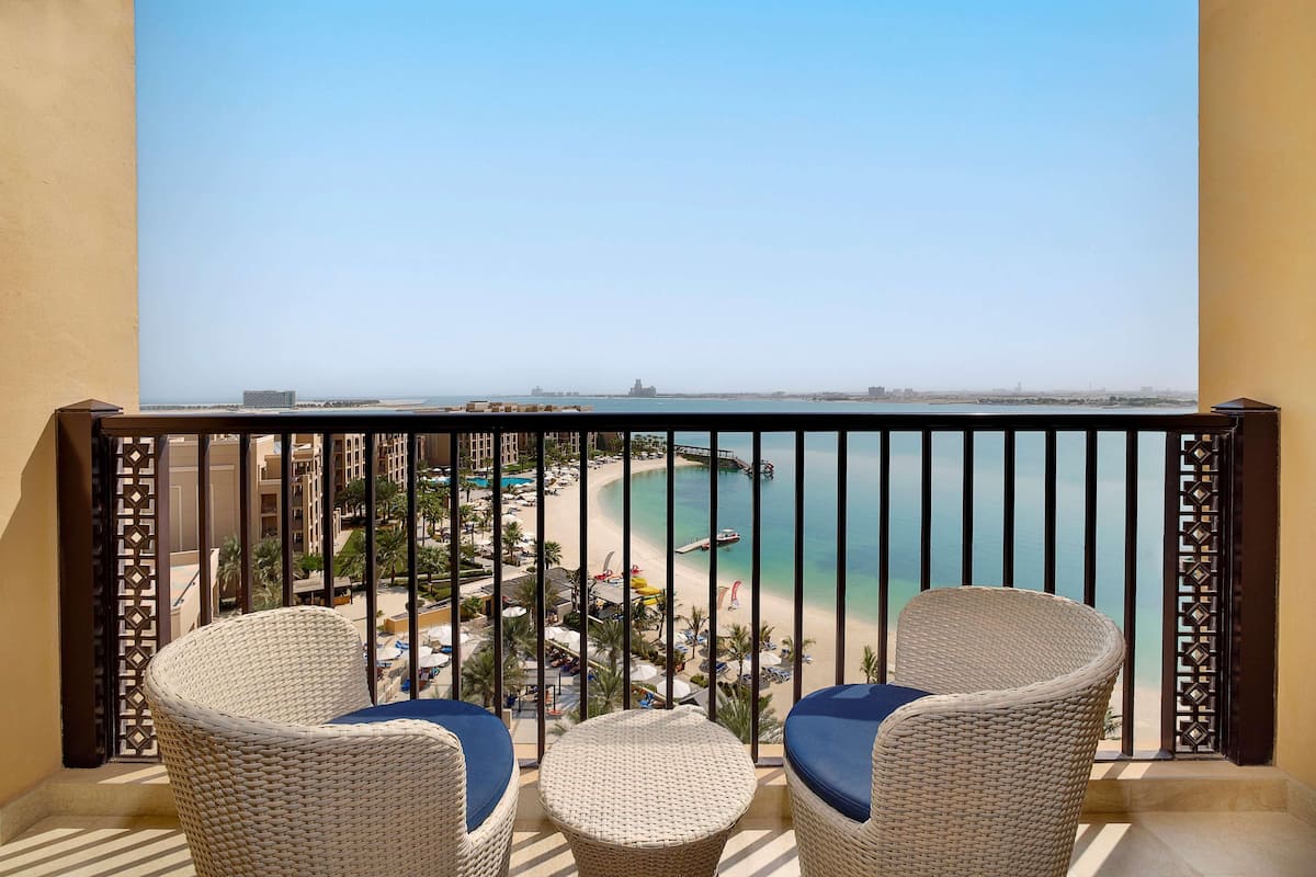 Een balkon met rieten stoelen en een tafel, met uitzicht op een strand en een pier.