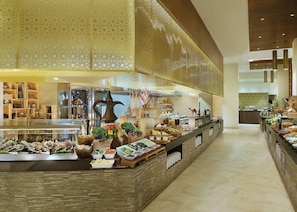 A buffet area with various food items and a kitchen in the background. - Doubletree by Hilton Resort & Spa Marjan Island (Ras Al Khaimah)