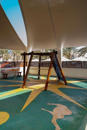 An outdoor play area with a swing set, benches, and a colorful play mat. - Doubletree by Hilton Resort & Spa Marjan Island (Ras Al Khaimah)