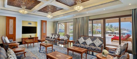 A spacious lounge with sofas, armchairs, and tables, a large TV, and a view of the outdoors.