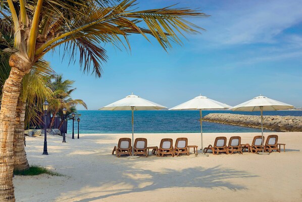 A beach with lounge chairs and umbrellas, palm trees, and a rocky shoreline.