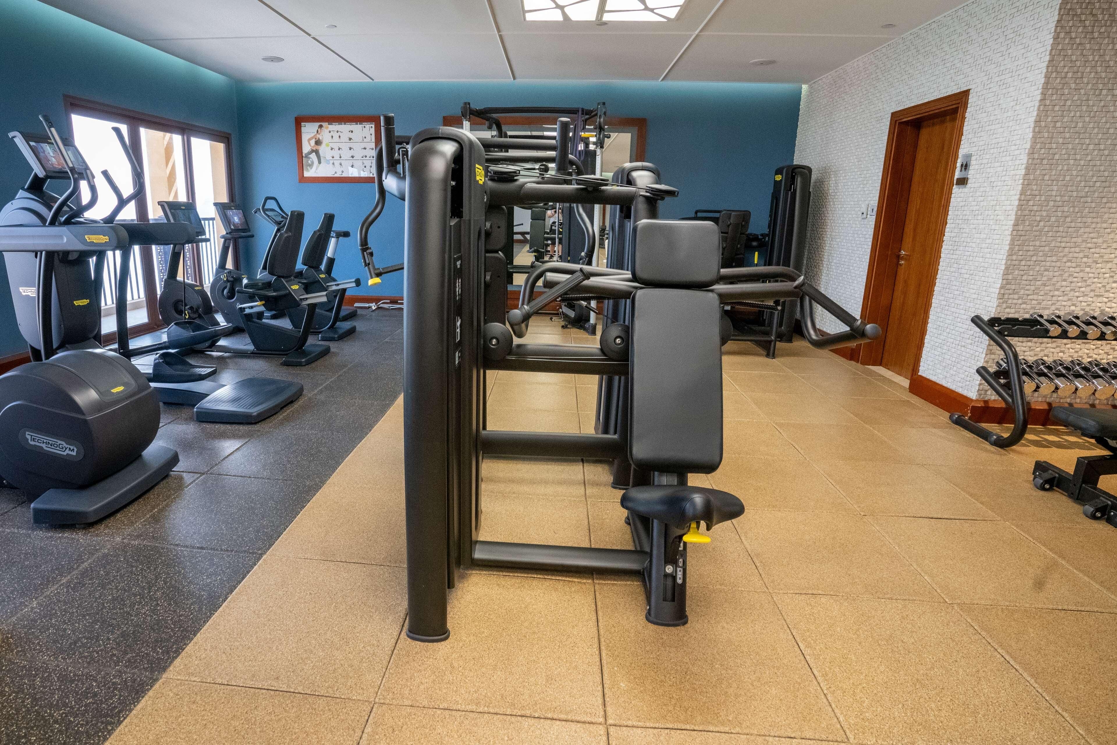 A gym with exercise equipment, a wall with a fitness chart, and a door.