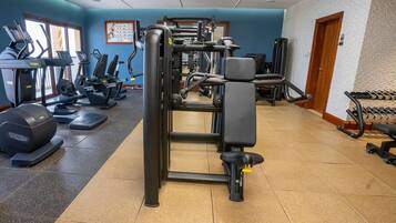 A gym with exercise equipment, a wall with a fitness chart, and a door.