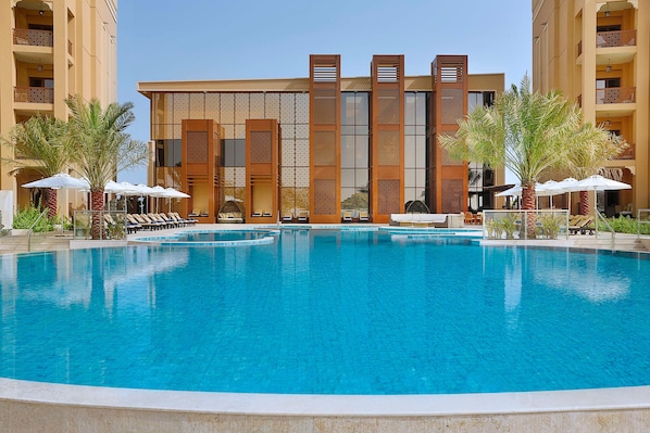 A hotel with a large swimming pool, sun loungers, and palm trees. - Doubletree by Hilton Resort & Spa Marjan Island (Ras Al Khaimah)