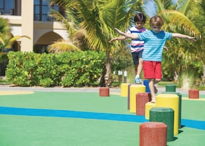 Two children playing on a colorful obstacle course with palm trees and a building in the background. - Doubletree by Hilton Resort & Spa Marjan Island (Ras Al Khaimah)