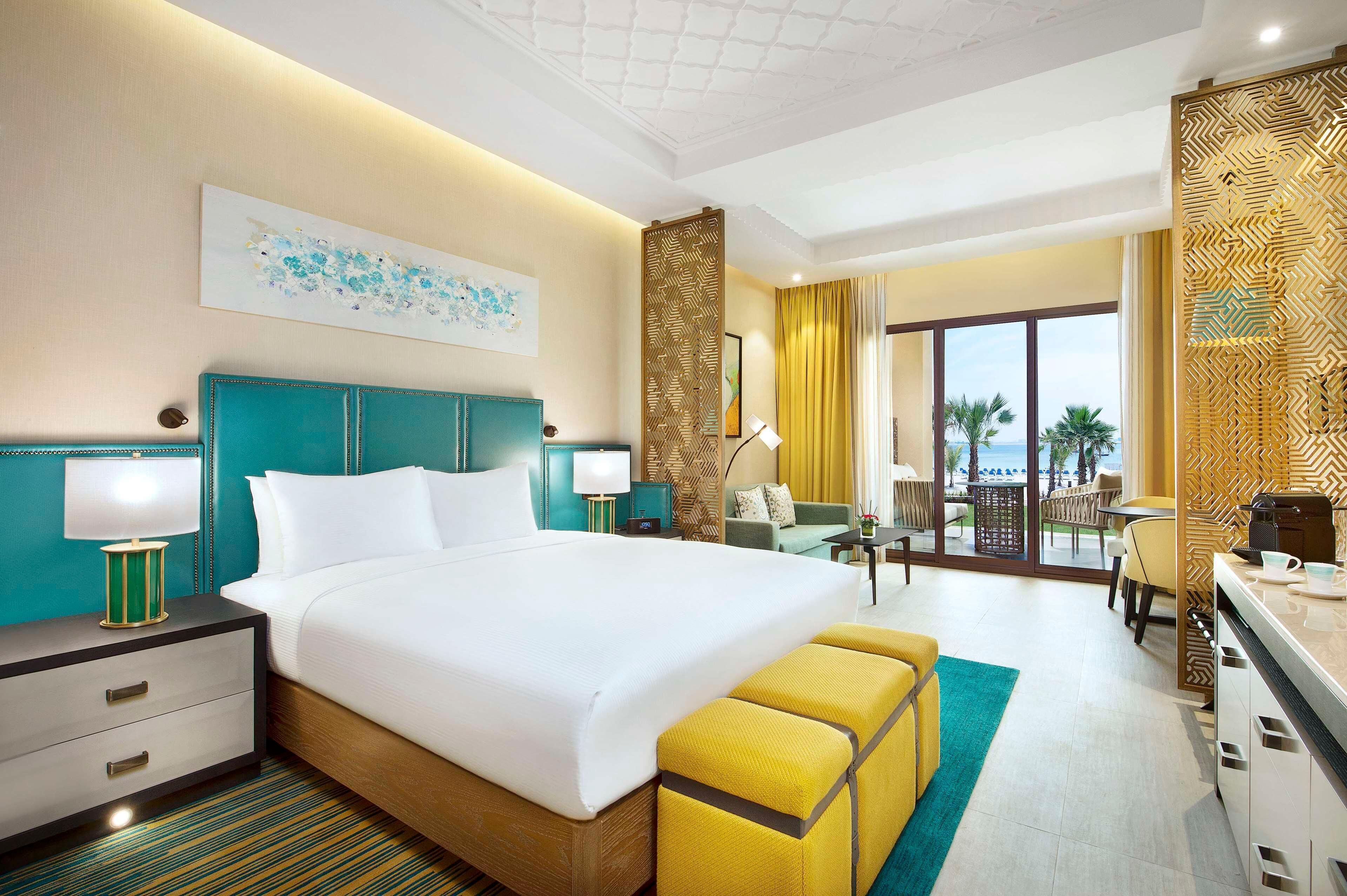 Une chambre d’hôtel comprenant un lit, des tables de chevet, un bureau, une chaise, un canapé, un balcon avec vue et un panneau décoratif mural.