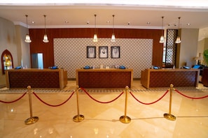 A reception area with three counters, a patterned wall, and hanging lights. - Doubletree by Hilton Resort & Spa Marjan Island (Ras Al Khaimah)