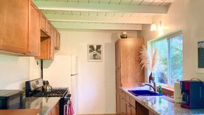 A kitchen with wooden cabinets, a stove, a refrigerator, a window with a view of trees, and a picture on the wall. - 50+ acre Nature Preserve with Ponds & Meadows: Azul Cottage Retreat (Mendocino)