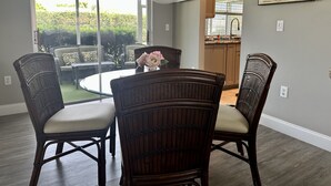 A dining area with a round table and four chairs, a chandelier, a sliding glass door leading to a patio, and a kitchen in the background.