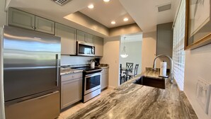 A modern kitchen with stainless steel appliances, a marble countertop, and a dining area with a chandelier.