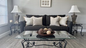 A living room with a dark grey sofa, two matching side tables, a glass coffee table, and a framed picture on the wall.