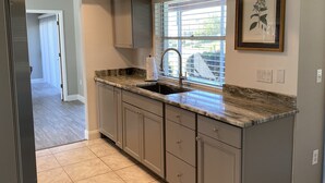 A kitchen with a granite countertop, a stainless steel sink, and light gray cabinets.