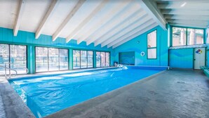 Une piscine intérieure avec un sol et des murs bleus, de grandes fenêtres et un plafond en bois.