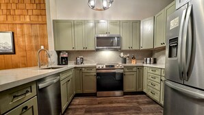 Une cuisine avec des meubles de couleur verte, des appareils électroménagers en acier inoxydable, un lave-vaisselle et un plancher en bois.