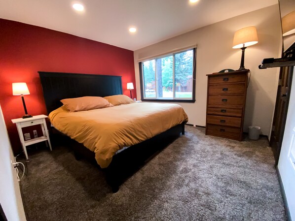 A bedroom with a bed, two bedside lamps, a dresser, and a window with a view of trees.