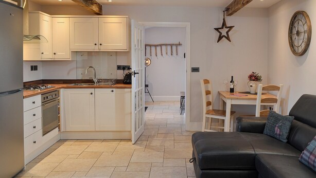 A modern kitchen with white cabinets, a built-in oven, and a dining area with a wooden table and chairs.