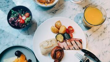 A breakfast setting with various dishes including toast, grilled meat, vegetables, and fruit on a marble table.