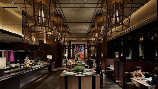 A modern restaurant with a central island, high ceiling, and hanging light fixtures.