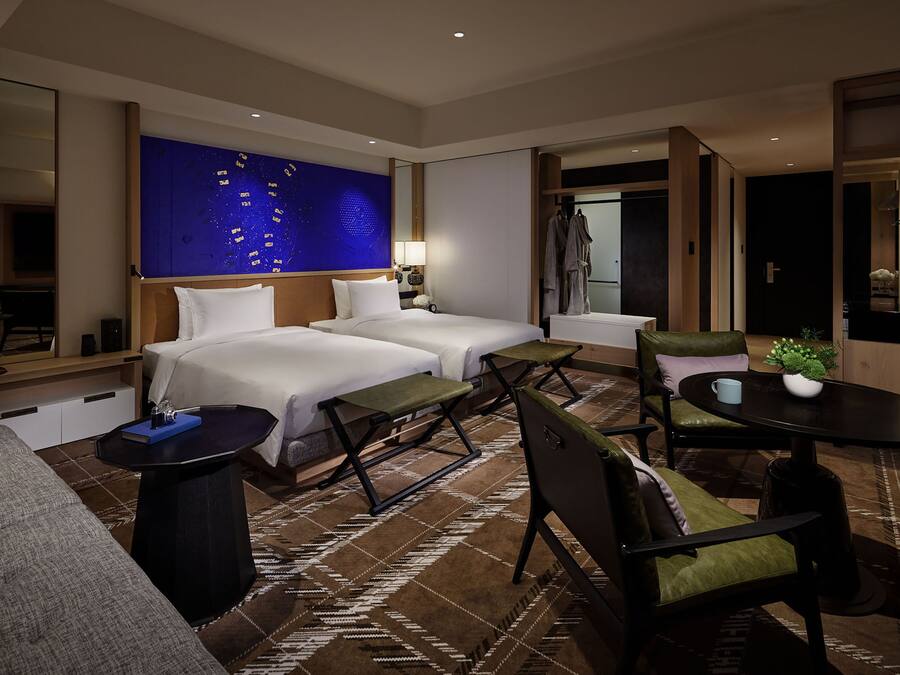 Une chambre d’hôtel avec deux lits, un canapé, une table à manger et une grande œuvre d’art bleue accrochée au mur.