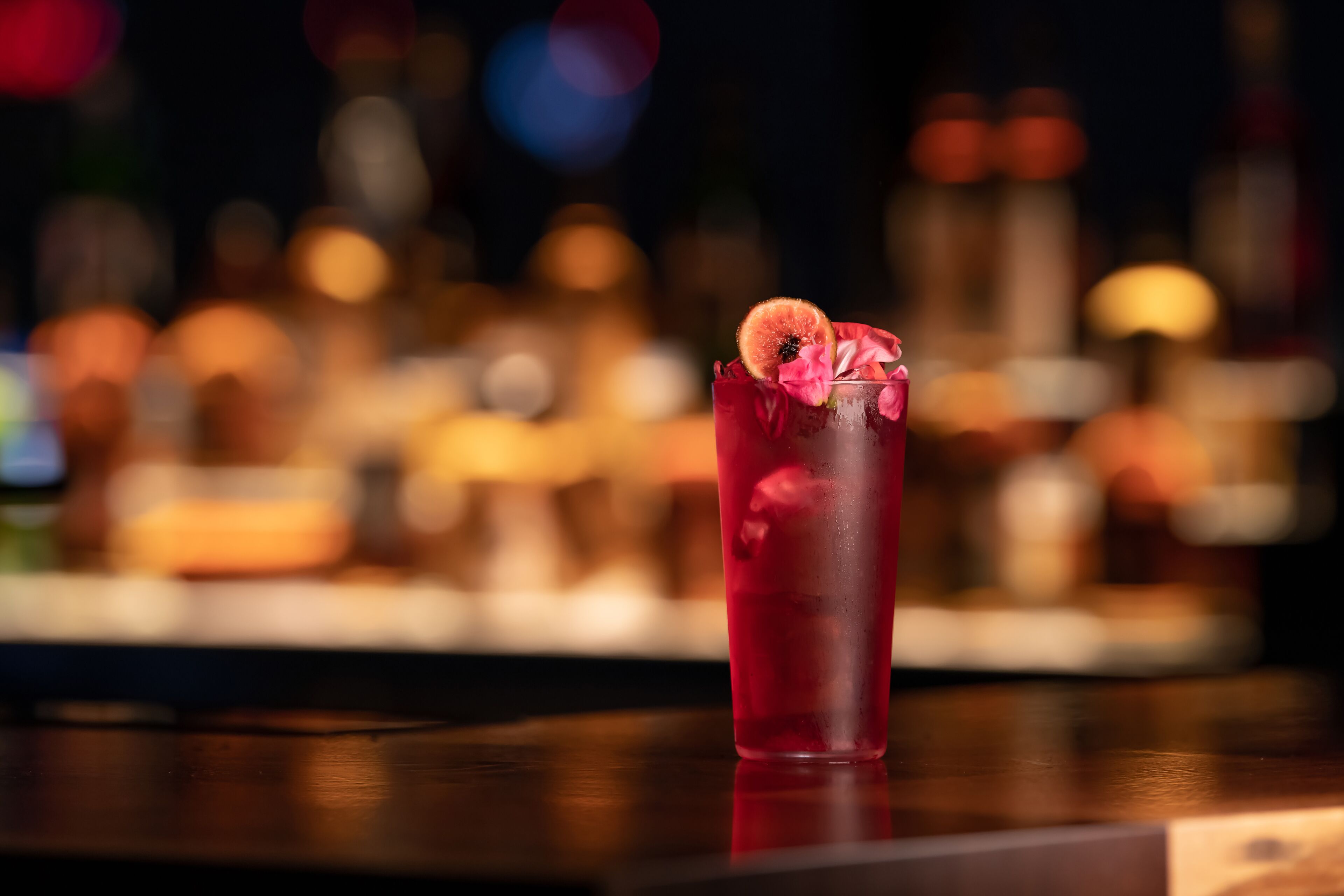 Eine Bar, in der ein Glas mit rotem Getränk, verziert mit einer Blume und einer Fruchtscheibe, steht.