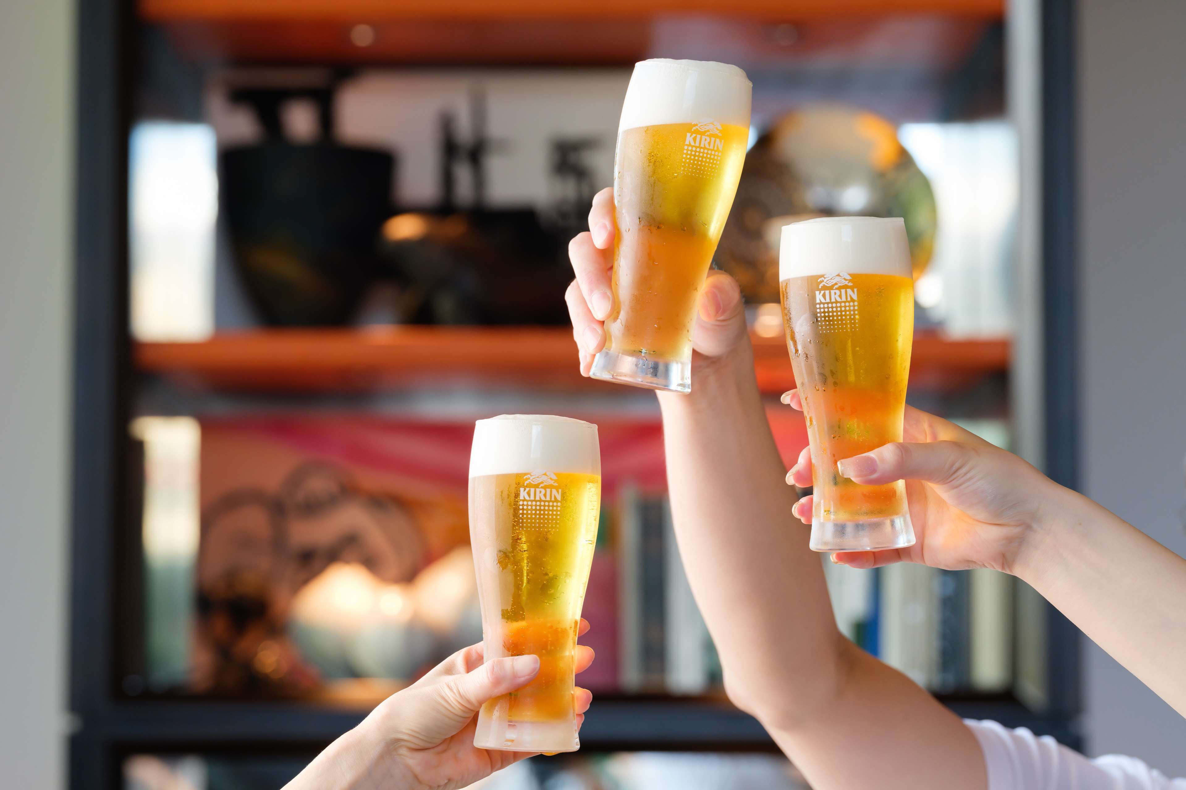 Three people holding up glasses of beer with a bookshelf in the background.