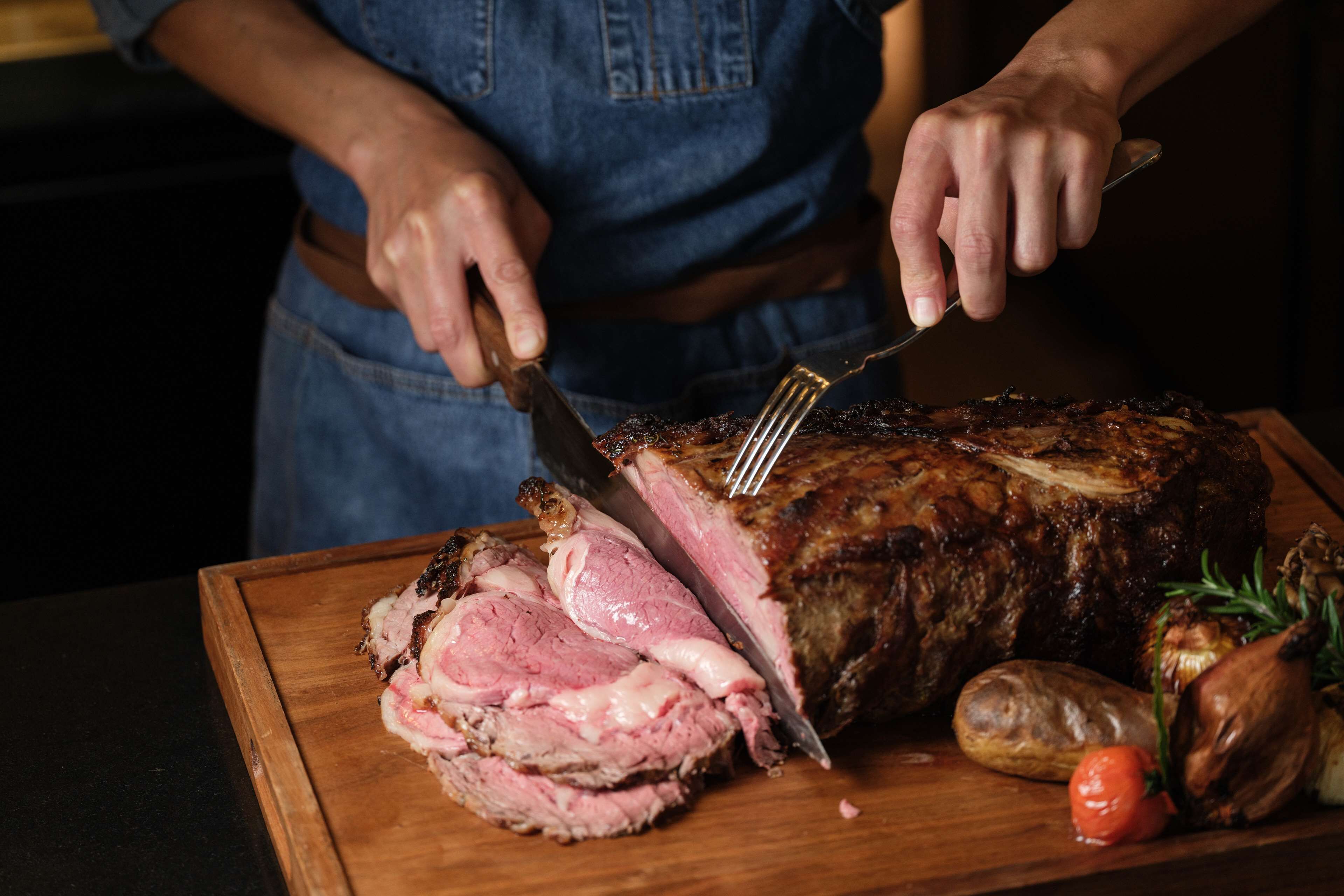 Una persona cortando un gran asado sobre una tabla de madera.