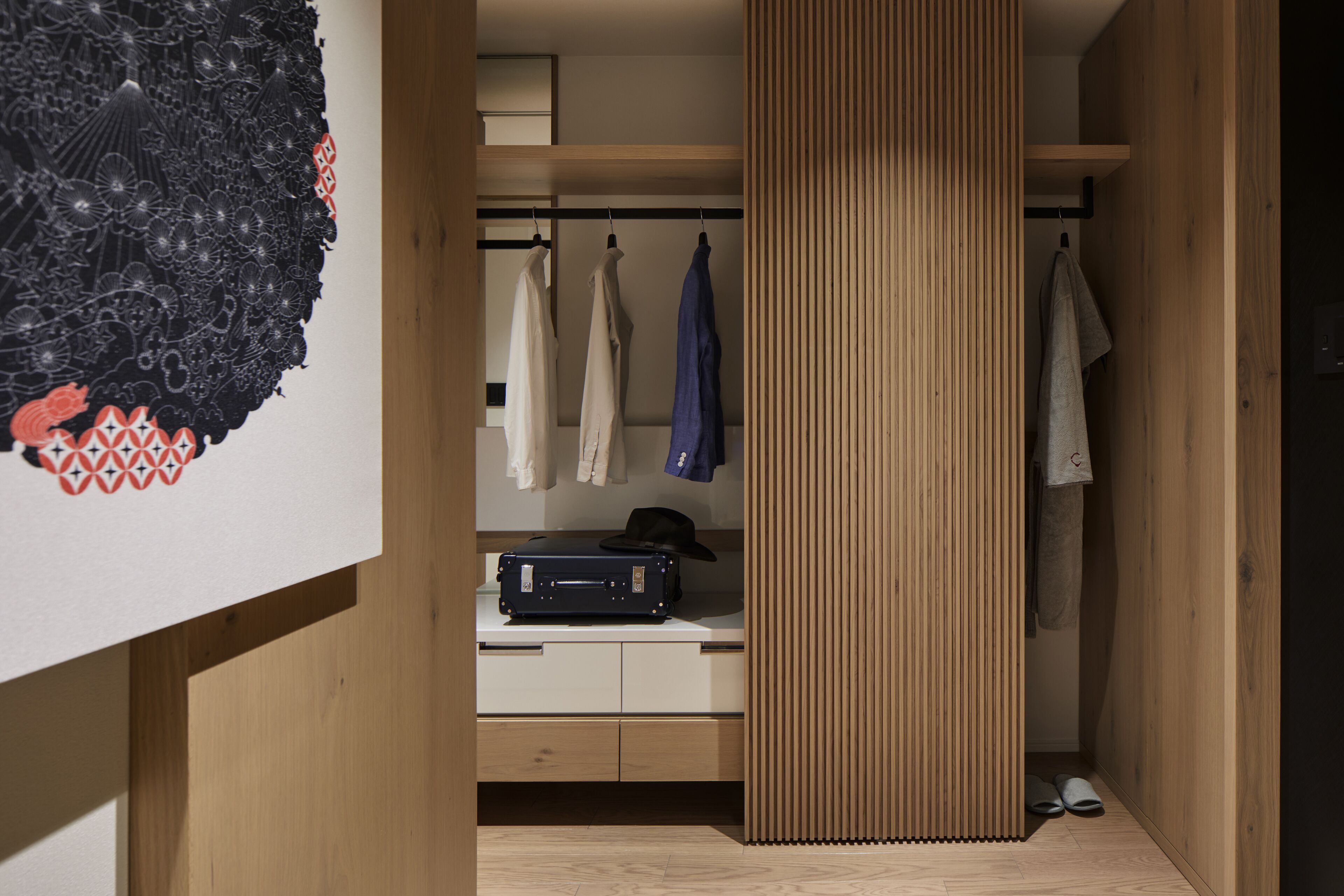 Una habitación moderna con un armario de madera, un escritorio con una maleta y un perchero.