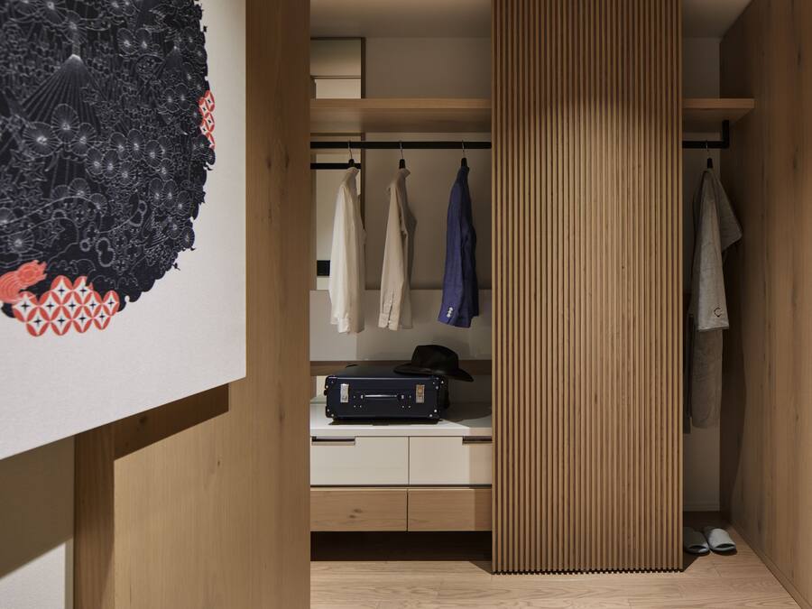 Una habitación moderna con un armario de madera, un escritorio con una maleta y un perchero.