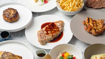 A variety of grilled meats and sides on plates, including steak, chicken, and a burger.