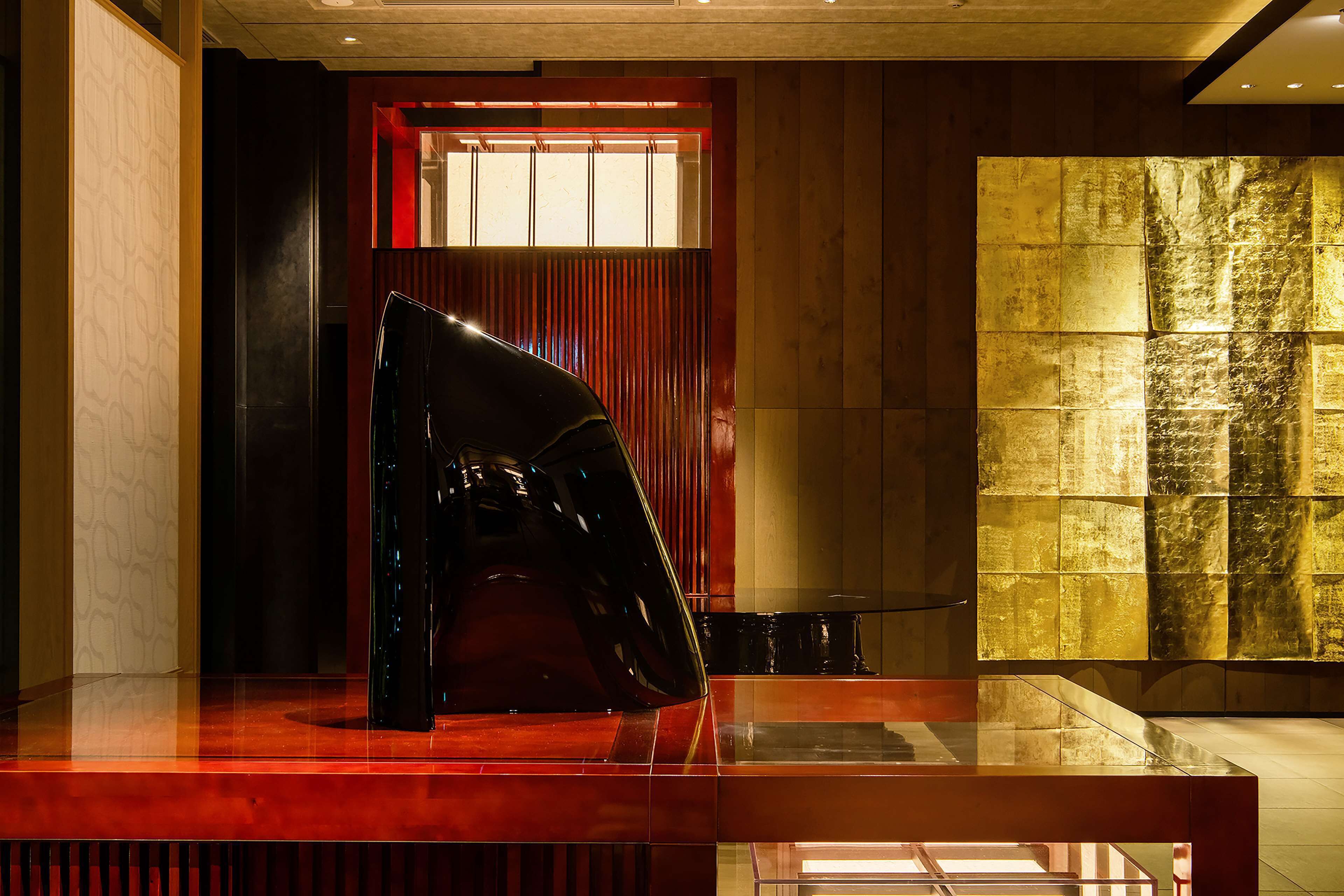 A modern interior with a glass table, a reflective sculpture, and a textured wall.