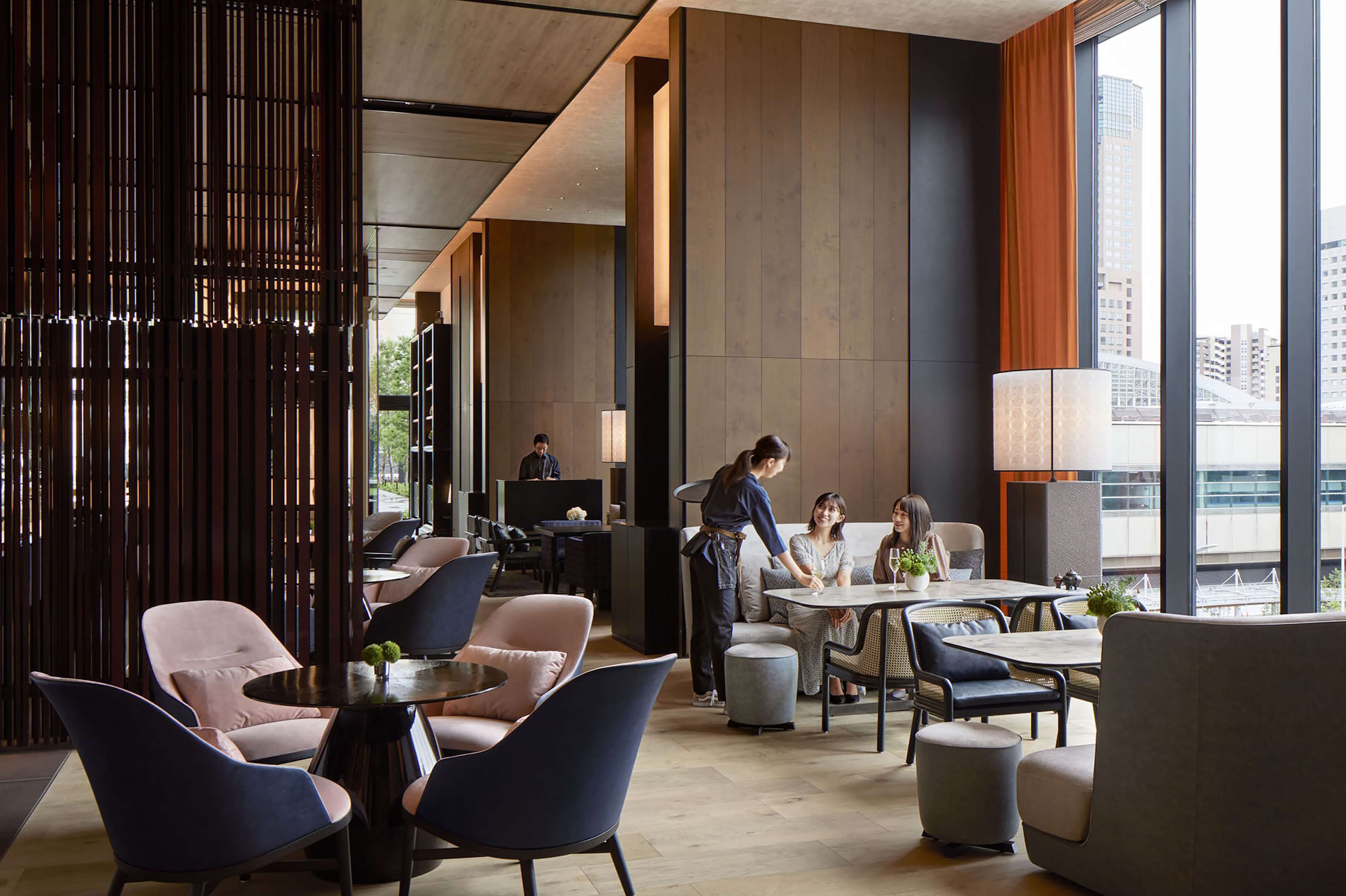 A modern hotel lobby with seating areas, a reception desk, and large windows offering city views.