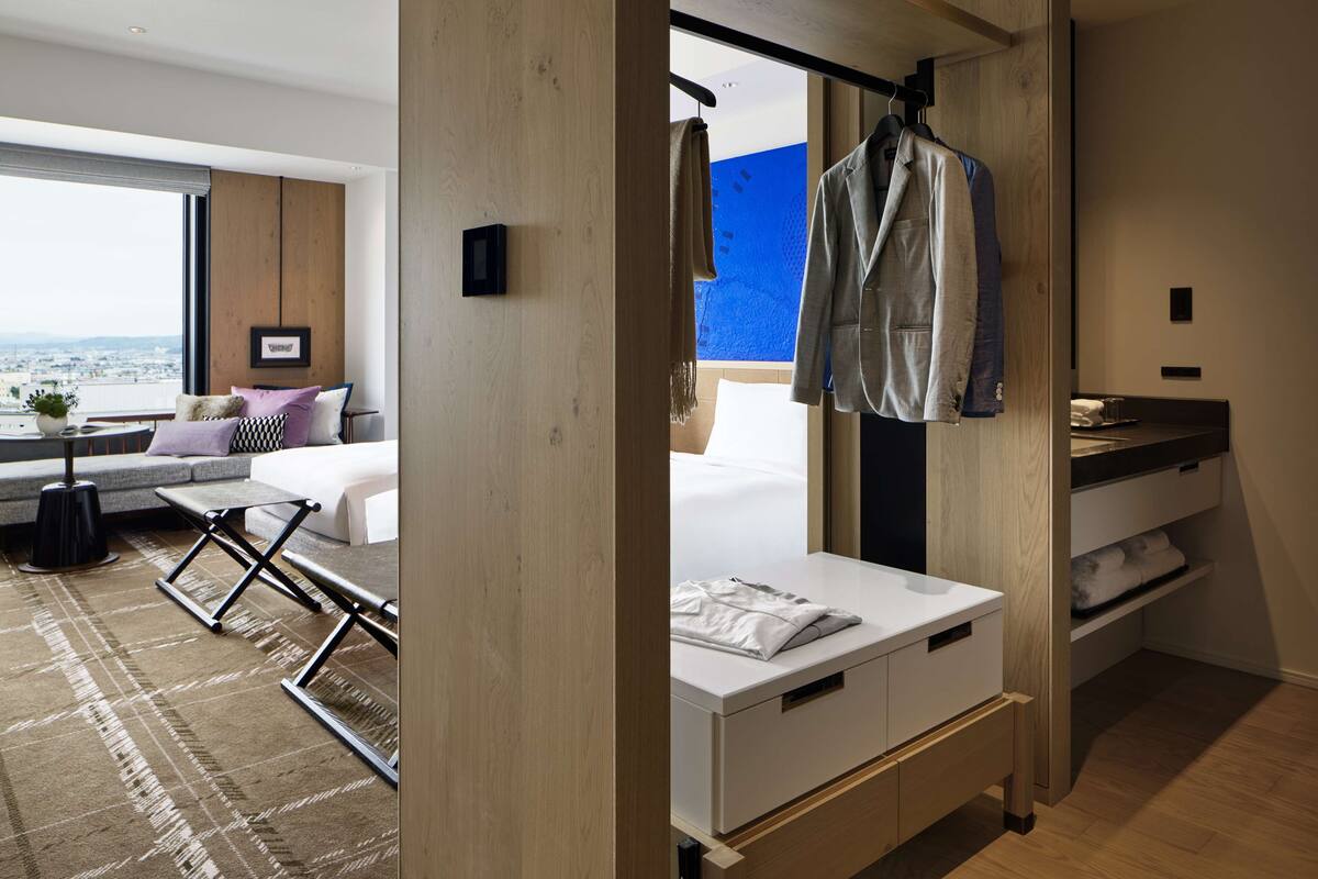 Ein modernes Hotelzimmer mit großem Fenster, einem Bett und einer Sitzecke mit Ausblick, sowie einem Badezimmer mit Handtuchhalter.