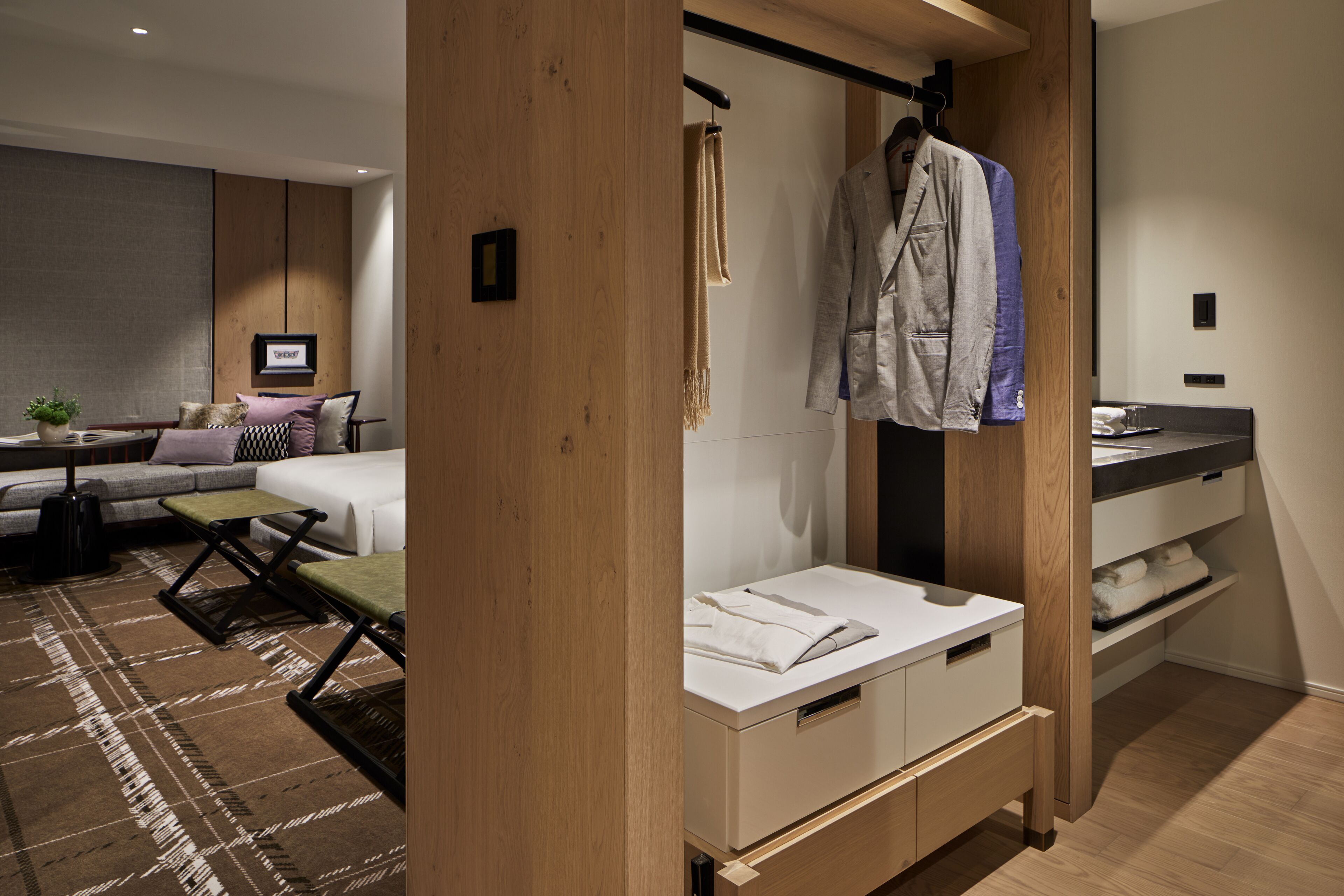 A modern hotel room with a bed, a sofa, a small table, and a desk area.