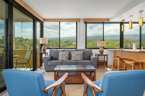 A modern living room with a sofa, two armchairs, a coffee table, and a view of the countryside through large windows. - 414 - Gorgeous 2 Bedroom Oceanfront property with A/C! (Kihei)