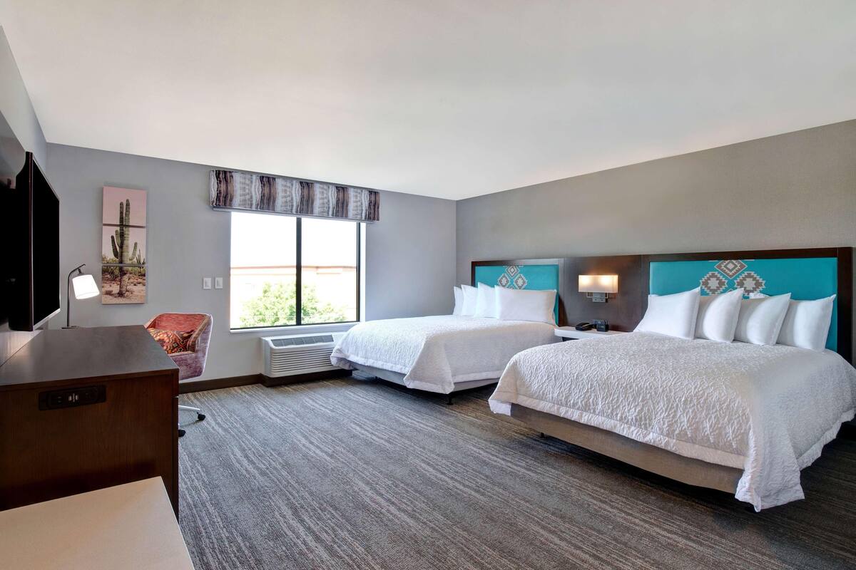 Une chambre d’hôtel avec deux lits, un bureau, une chaise, une télévision et une grande fenêtre.