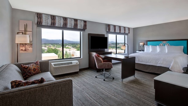 A hotel room with a large bed, a desk with a TV, a sofa, and a view of the city.