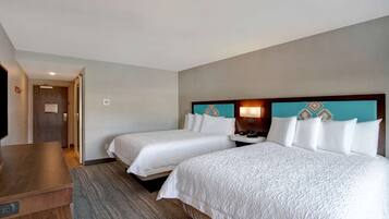 A hotel room with two beds, a wooden desk, and a television.