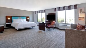 A hotel room with a bed, desk, chair, and large windows.
