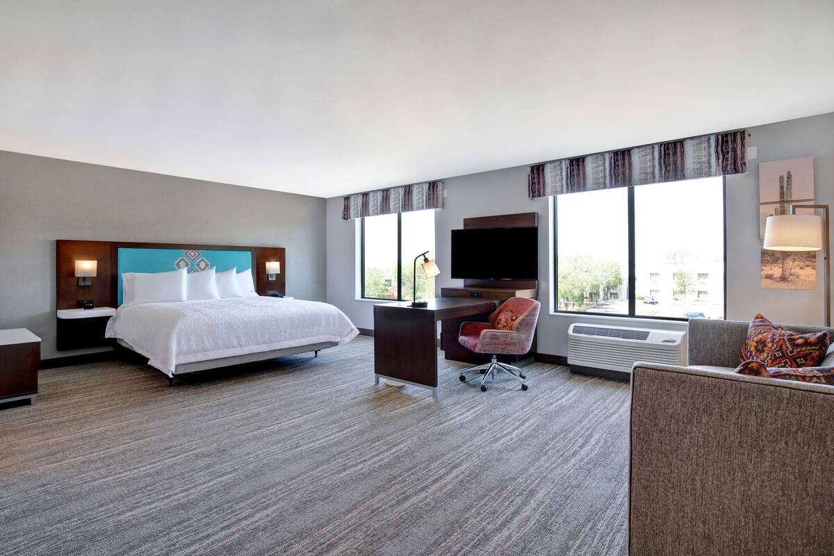 Une chambre d’hôtel avec un lit, un bureau, une chaise et de grandes fenêtres.