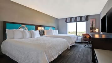 Habitación de hotel con dos camas, un escritorio, una silla, un televisor y una ventana con vistas.