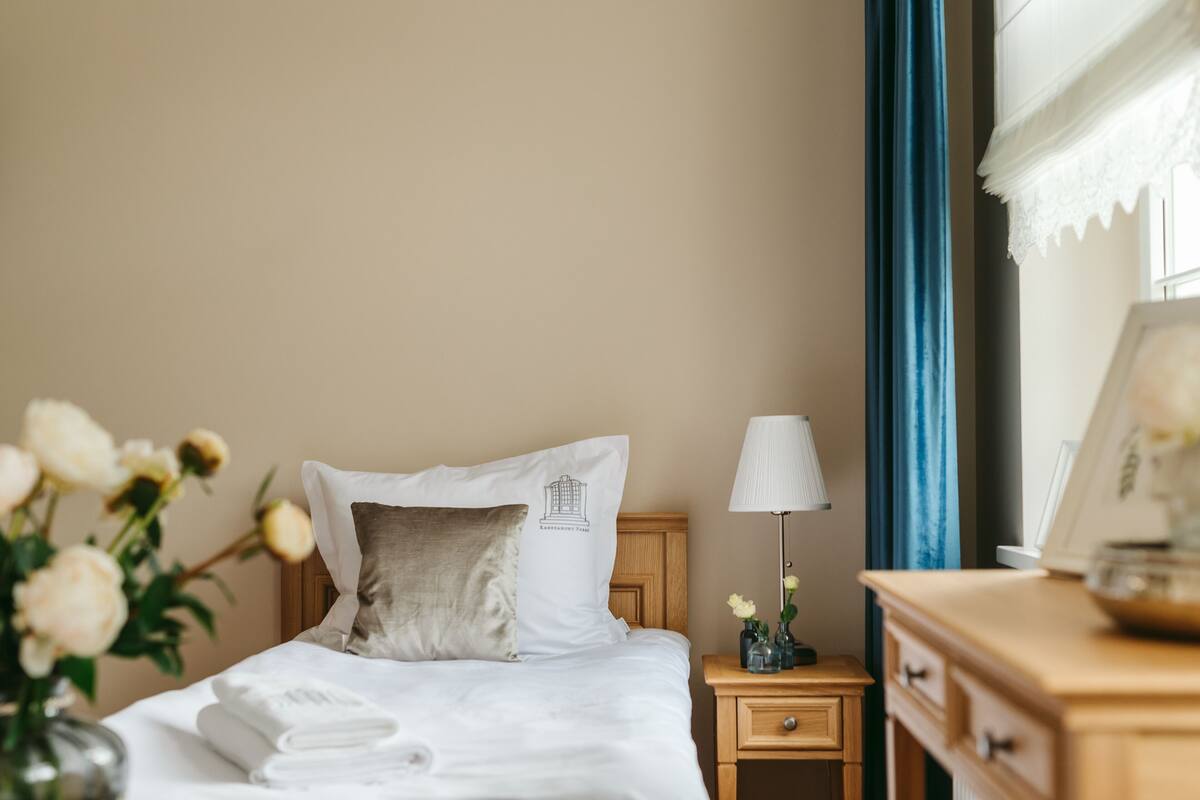 Ein ordentlich bezogenes Bett mit Kissen, ein Nachttisch mit Lampe und eine Vase mit Blumen.