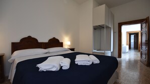 A hotel room with a neatly made bed, a nightstand with a lamp, and a wooden wardrobe.