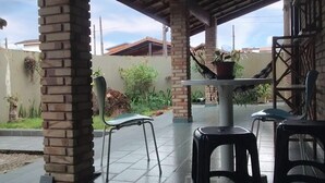An outdoor patio area with brick pillars, a table with a potted plant, and two black plastic chairs. - House for rent in the Center of Ubatuba (Ubatuba)