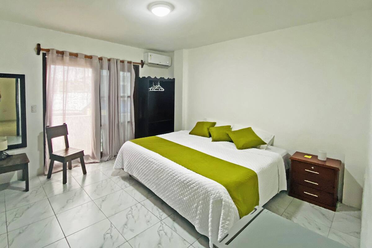 A bedroom with a bed, a chair, a dresser, and a mirror.