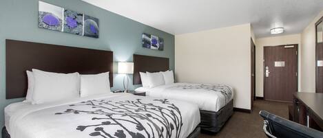 A hotel room with two beds, a desk, a chair, a mirror, and artwork on the wall.