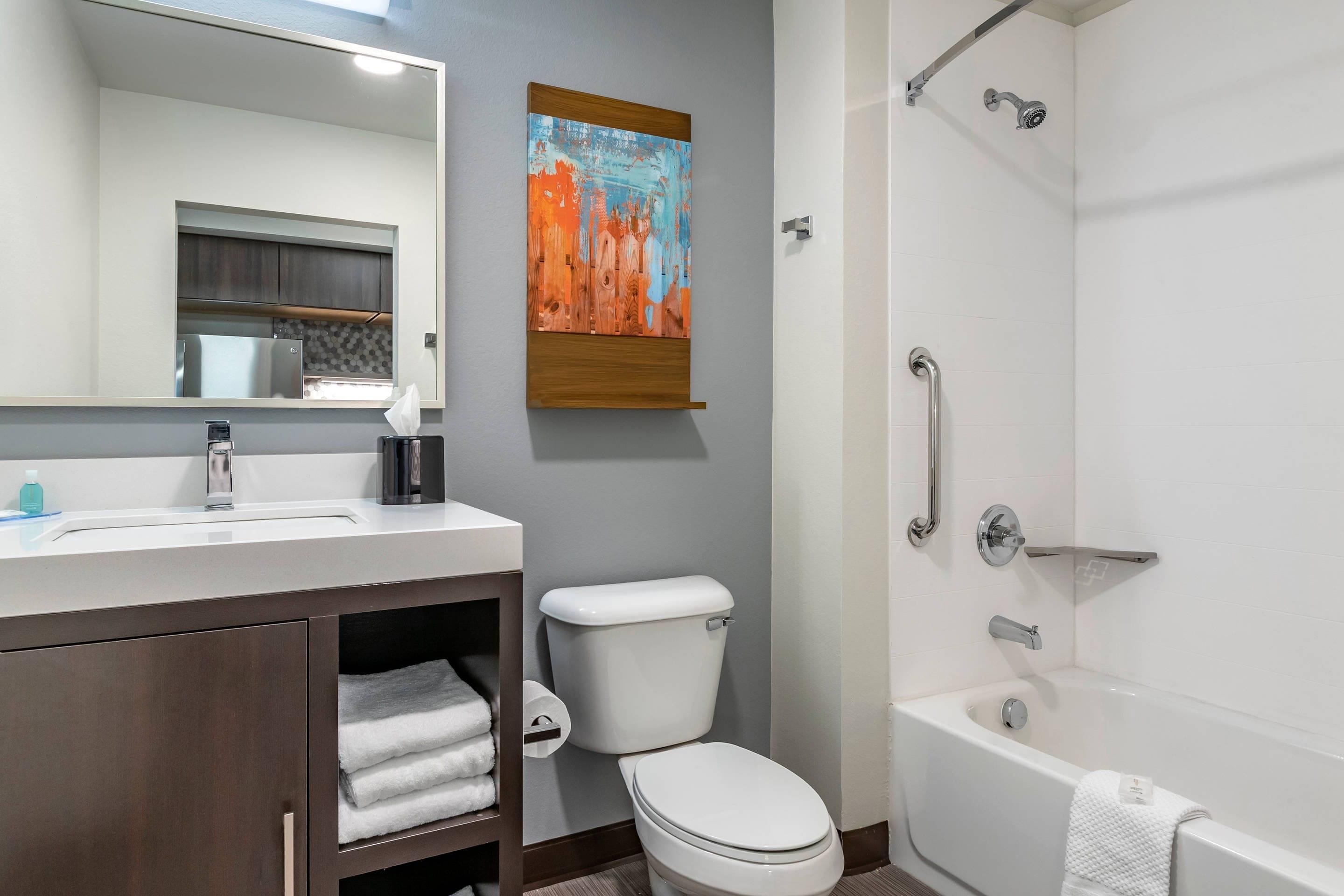 A modern bathroom with a white toilet, a bathtub, a shower with a grab bar, a sink with a mirror, and a towel rack.