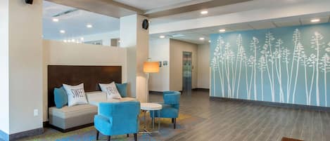 A modern lobby with a sofa, chairs, a lamp, and a wall with a floral pattern.